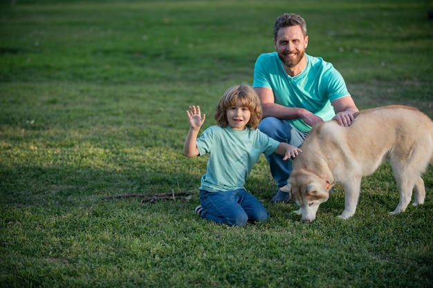 Son and father as family with dog playing together in summer park on grass child with her pet friend