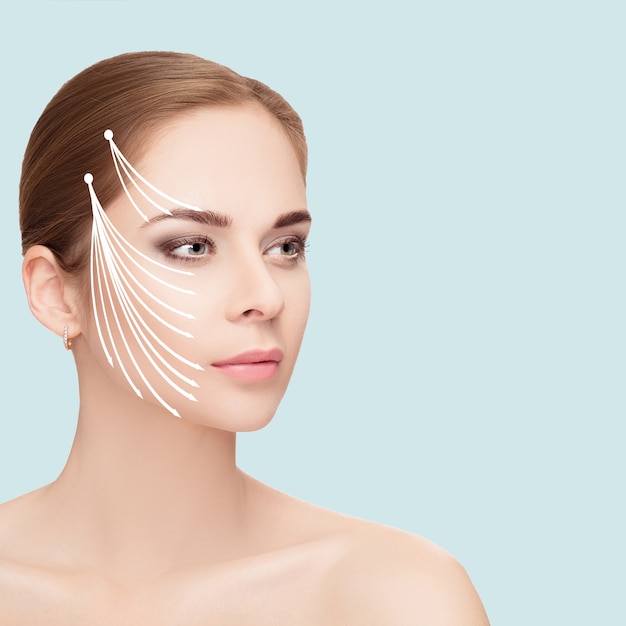 Spa portrait of attractive woman with arrows on her face over blue background. Face lifting concept. Plastic surgery treatment, medicine