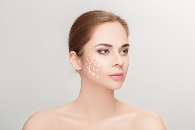 Spa portrait of attractive woman with arrows on her face over grey background. Face lifting concept. Plastic surgery treatment, medicine