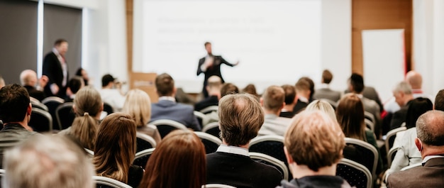 Foto oratore che tiene un discorso in una sala conferenze in un evento aziendale vista posteriore di persone irriconoscibili in