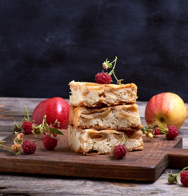 Square pieces of apple pie are stacked on brown wooden board