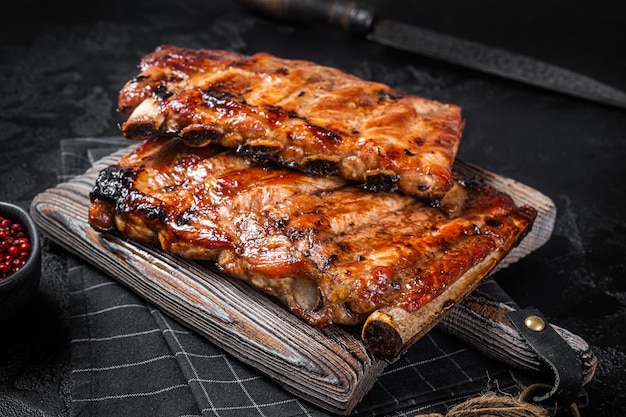 Stack of grilled pork ribs in BBQ sauce on a chopping board Black background Top view