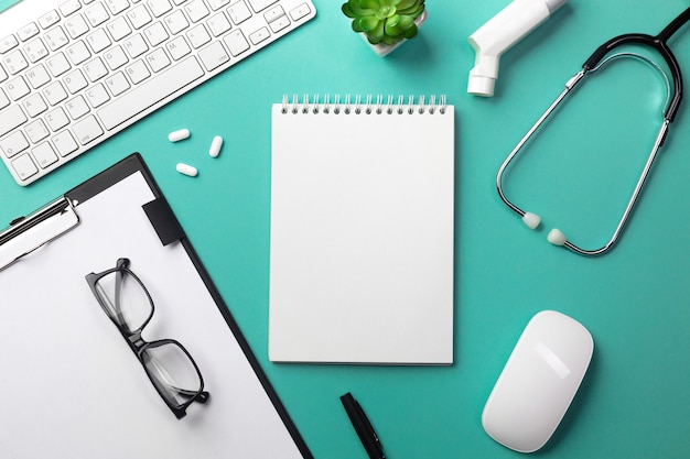 Stethoscope in doctors desk with notebook, pen, keyboard, mouse and pills