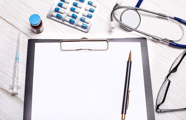 Stethoscope, pills, syringe, pen, medicine vials and glasses near a sheet of paper with copy space.