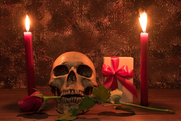 Still life painting photography with human skull, present, rose and candle on wooden table