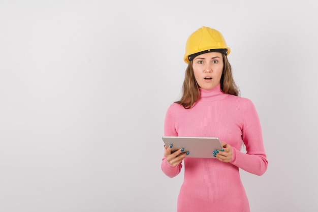 Surprised engineer girl is looking at camera by holding planshet computer on white background