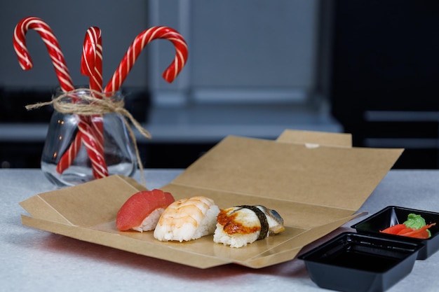 Photo sushi with tuna shrimp and eel lies in a cardboard box on the table in the kitchen christmas concept festive decorations in the form of candles figurines and sweets