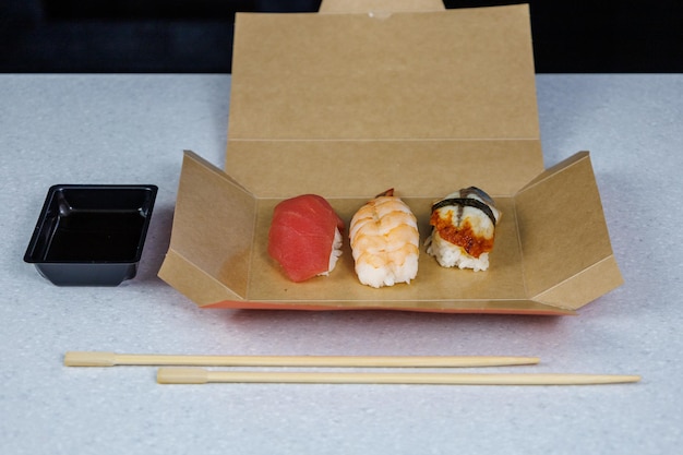 Photo sushi with tuna shrimp and eel lies in a cardboard box on the table in the kitchen fast food concept