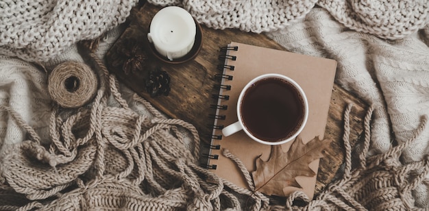 Sweaters and cup of tea with notebook, candle and knitting clothes