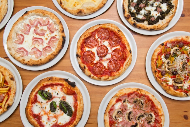 Tafel met pizza's van verschillende smaken, uitzicht van bovenaf.