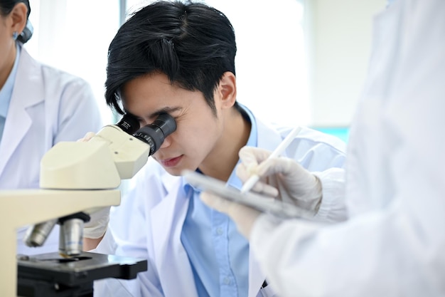 Photo talented asian male scientist looking under the microscope working with his colleagues