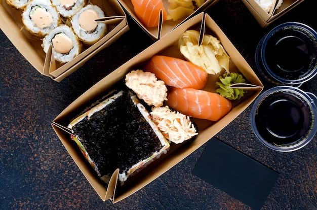 Photo tasty sushi rolls in disposable kraft paper boxes, sauces