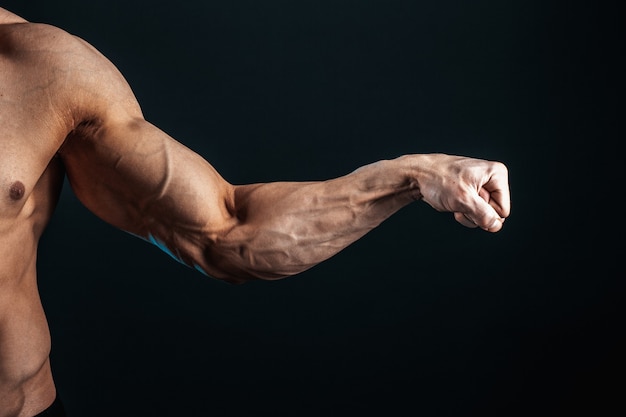 Photo tense arm clenched into fist, veins, bodybuilder muscles on a dark space, isolate