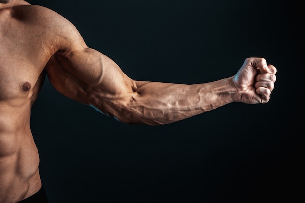 Photo tense arm clenched into fist, veins, bodybuilder muscles on a dark space, isolate