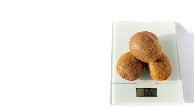 Three ripe unpeeled kiwi fruits on the scales on a white background Kiwi is a natural dietary product a source of vitamins and antioxidants Healthy vegetarian food concept