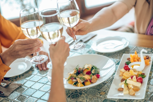 Photo toast. close up picture of galsses with wine in hands of friends