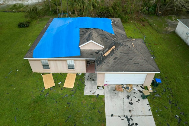 Top view of leaking house roof covered with protective tarp sheets against rain water leaks until replacement of asphalt shingles Damage of building rooftop as aftermath of hurricane Ian in Florida