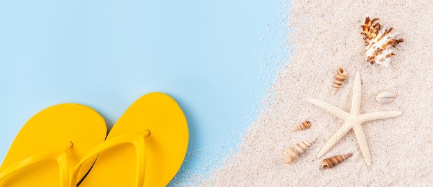 Top view with copy space of yellow sandals with starfish and shells sand on blue background