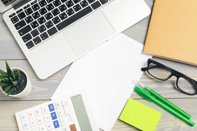 Top view of wooden desktop with glasses and stationery items close up. Mock up