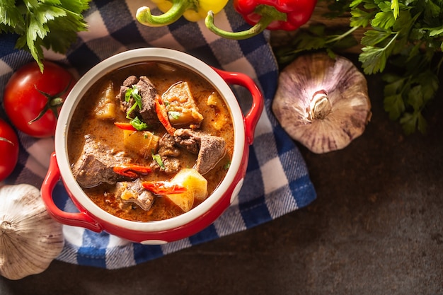 Photo top views of bowl of goulash soup with meat, potatoes and chillies.