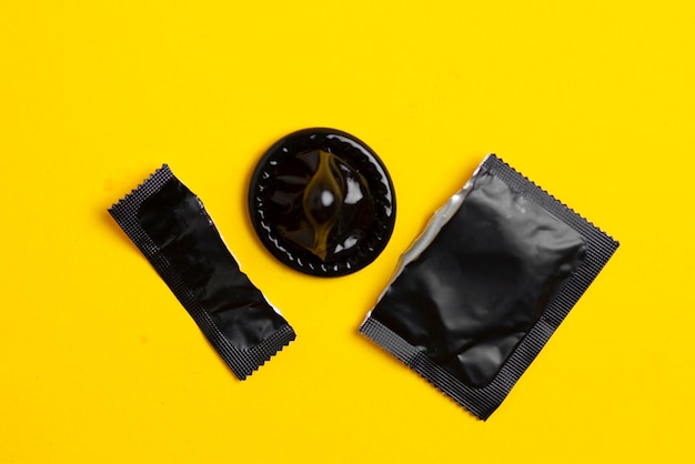 Photo torn black pack of a condom lies on a yellow background the concept of safe sex