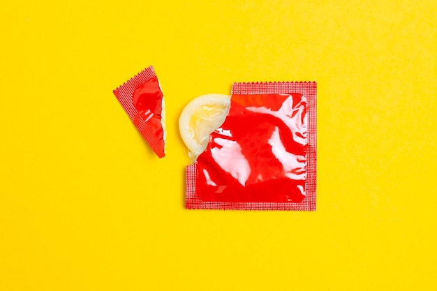 Photo torn pack of a condom lies on a yellow background the concept of safe sex