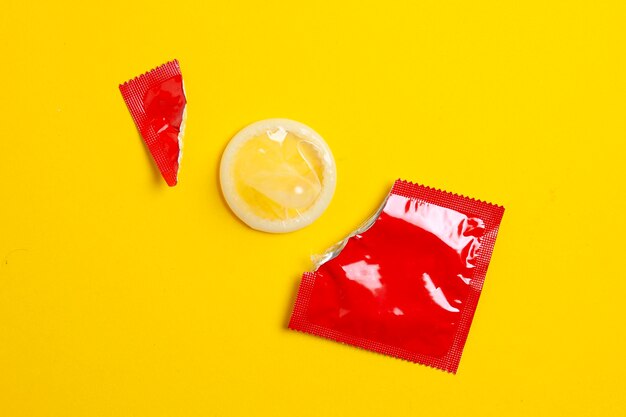 Photo torn red pack of a condom lies on a yellow background the concept of safe sex