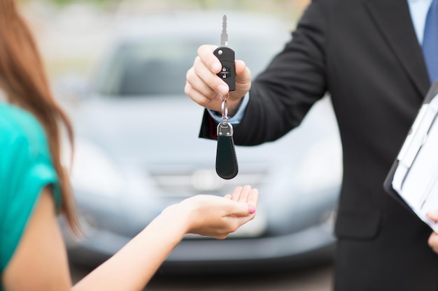 transportation and ownership concept - customer and salesman with car key outside