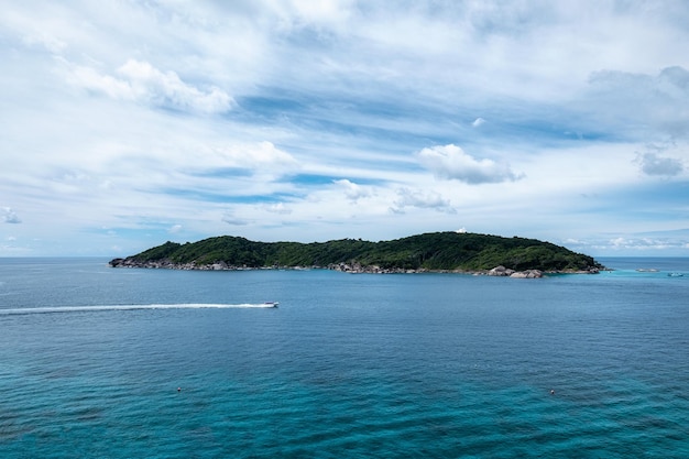 Tropical sea with tiny island and boat sailing on sunny day