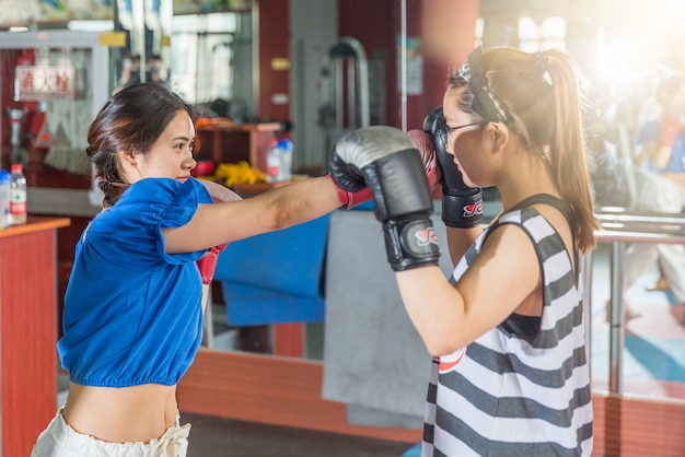 Two female boxing friends exercising in gymnasium.