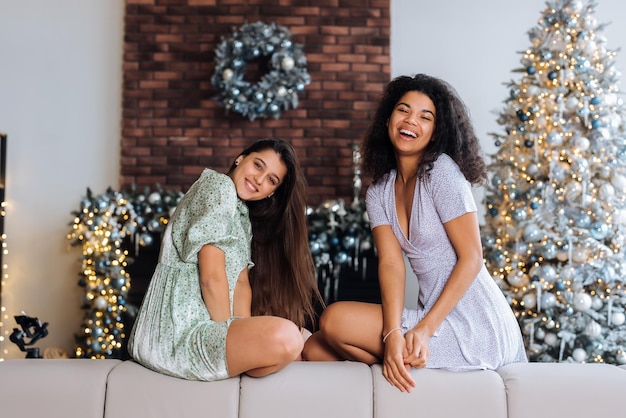 Two girls sit on the back of the sofa look at the cameras and smile at home