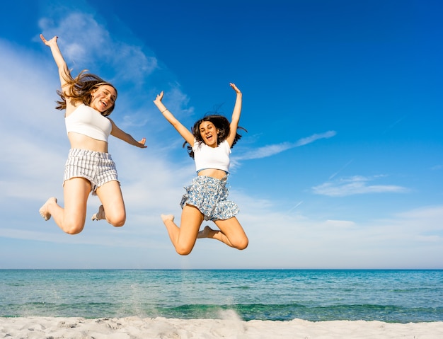 Photo two happy girls jumping together on tropical beach enjoying summer vacation