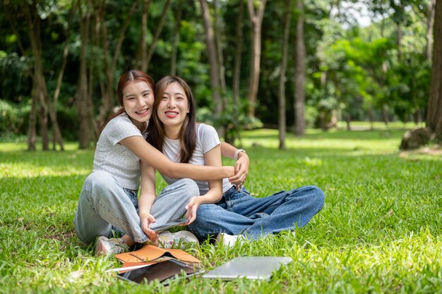 Foto due belle amiche asiatiche si abbracciano e sorridono mentre sono sedute insieme nel parco.