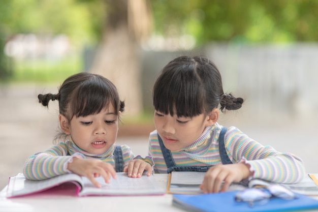 Photo two student little asian girls reading the book on table