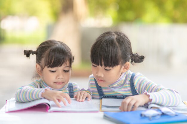 Photo two student little asian girls reading the book on table