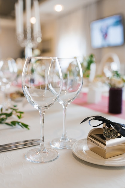 Two wine glasses are on the festive Banquet table and next to it is a box of sweets-bonbonniere