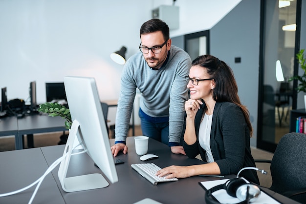 Two young business people looking at computer monitor. Working on a project together.