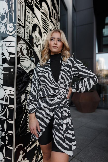 Urban fashion beautiful woman model in a stylish zebra dress stands near a bw print near a building in the city