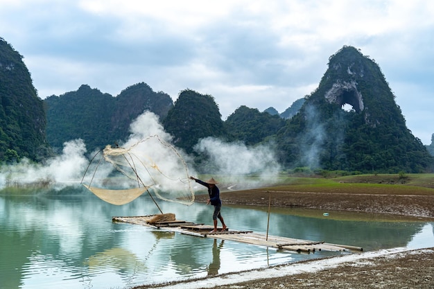 Photo view of fishermen casting his net on river in thung mountain in tra linh cao bang province vietnam with lake cloudy nature and camping outdoor travel and landscape concept