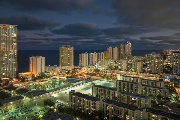 View from above of brightly illuminated high skyscraper buildings in downtown district of Sunny Isles Beach city in Florida USA American tourist urban district at night