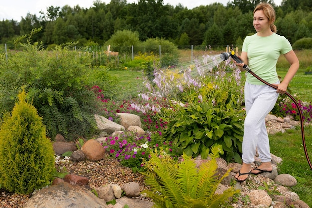 Vrouwelijke tuinman die bloemen in een bloembed met een tuinslang water geeft