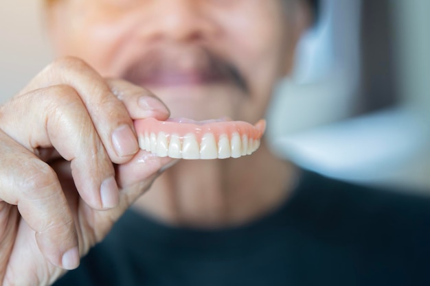 Waist up portrait of the old happy man in black tshirt showing model of human teeth