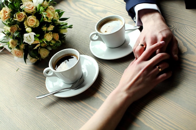 Wedding couple holding hands with cups of coffee at wooden table