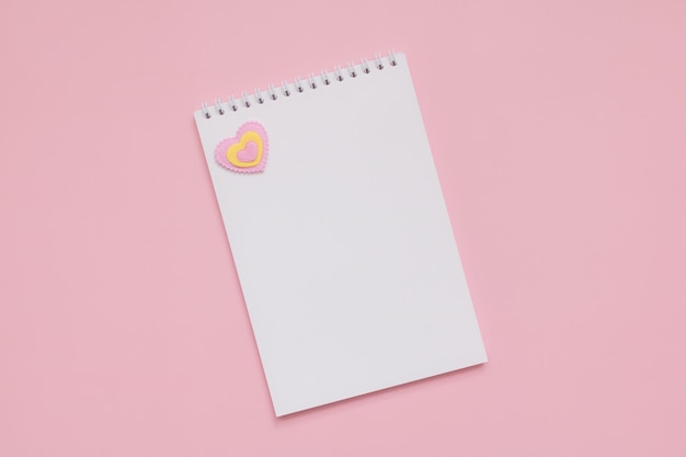 White blank notepad sheet, pink and yellow heart on a pink wall, Happy Valentines Day