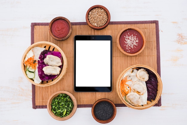 White blank screen digital tablet surround with sauce; chives and sesame seeds on placemat over texture backdrop