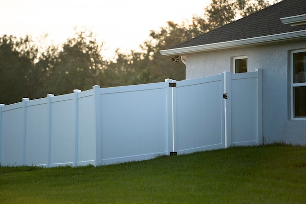 White vinyl picket fence on green lawn surrounding property grounds for backyard protection and privacy