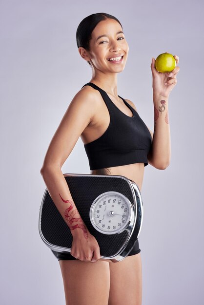 Photo woman apple and scale in studio portrait with pride for choice diet and results by white background girl person and happy with decision to lose weight with fruits detox and nutrition for health