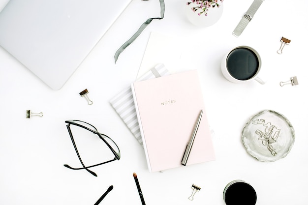 Woman modern home office desk with pastel pink notebook, glasses, coffee cup, wild flowers and accessories on white background