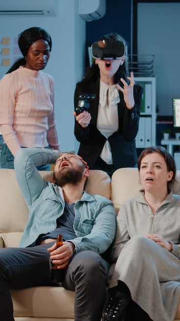 Woman playing video games with joystick and vr glasses, losing game play while colleagues cheering to do fun activity after work. Coworkers enjoying game on console television with entertainment