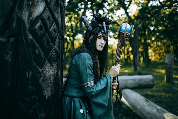 Woman-shaman with horns in green dress walk in forest